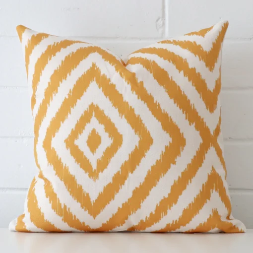 Gold patterned cushion cover in front of a white wall. It has a square size and is made from a linen material.