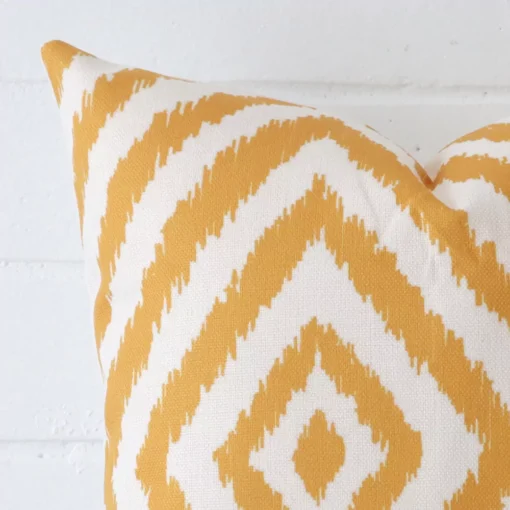 Square patterned cushion in gold colour sitting upright in front of a brick wall. It has been made from a quality linen material.