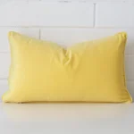 Velvet rectangle cushion in an upright position against a white brick wall. It is lemon yellow in colour.