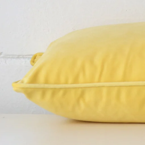 Rectangle cushion cover in lemon yellow colour sitting flat. The sideways viewpoint shows the seams of the velvet material.