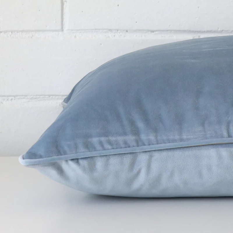 Square cushion cover in light blue colour sitting flat. The sideways viewpoint shows the seams of the velvet material.