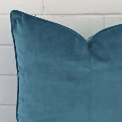 Close range image of light teal cushion. The square size and velvet material can be seen in detail.