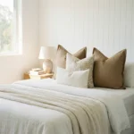 Lily cushions styled on bed with warm taupe, floral and textured neutral cushions.