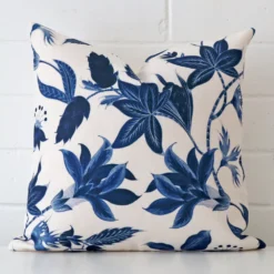 Floral cushion cover sits against a white wall. It is constructed from a superior looking linen material and has square dimensions.