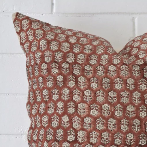 Square floral cushion sitting upright in front of a brick wall. It has been made from a quality designer material.