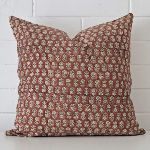 White wall with a floral cushion laying against it. It has a distinctive designer fabric has a square shape.