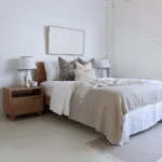 An airy white bedroom with 4 designer cushions sitting on a wooden bed.