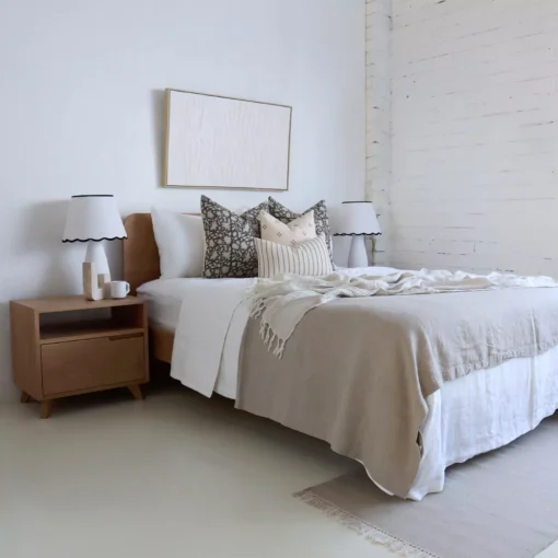 An airy white bedroom with 4 designer cushions sitting on a wooden bed.