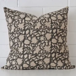 Square cushion with a floral design in an upright position against a white brick wall. It has been made from a quality designer material.