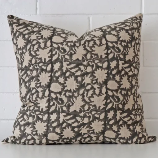 Square cushion with a floral design in an upright position against a white brick wall. It has been made from a quality designer material.