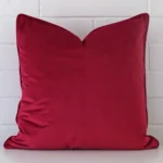 Square cushion cover in magenta colour sitting upright in front of a brick wall. It has been made from a quality velvet material.