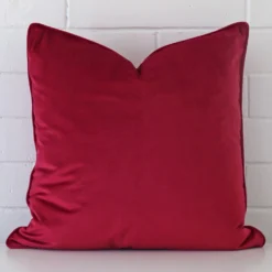 Square cushion cover in magenta colour sitting upright in front of a brick wall. It has been made from a quality velvet material.