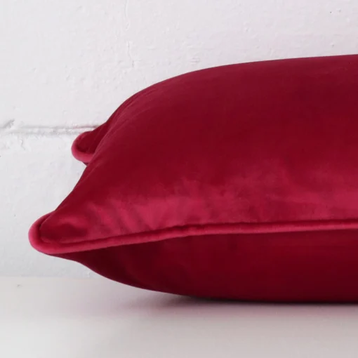 Magenta cushion cover laying sideways against brick wall. The rectangle size and velvet material are shown highlighting the seams.