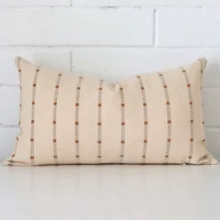 An attractive striped designer cushion in front of a white brick wall. It has a rectangle shape.
