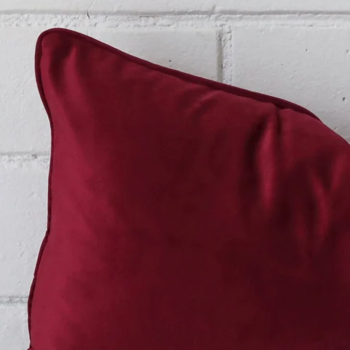 Close up view showing a corner of this velvet cushion in a rectangle size and with maroon colouring.
