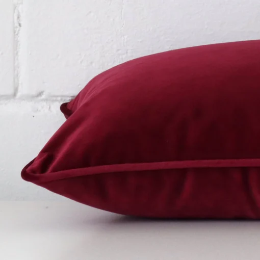 Maroon cushion laid horizontally. This perspective shows the edge of the velvet fabric and its rectangle shape.