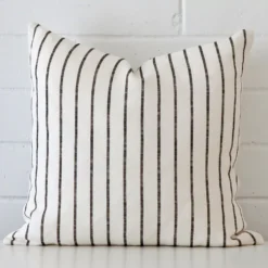 Striped cushion cover sits against a white wall. It is constructed from a superior looking linen material and has square dimensions.