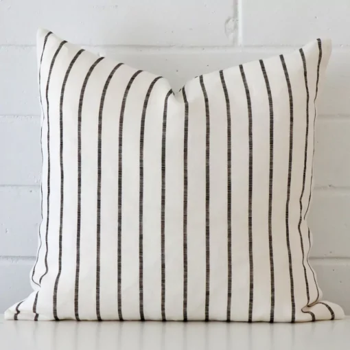 Striped cushion cover sits against a white wall. It is constructed from a superior looking linen material and has square dimensions.