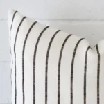 Corner section image showing features of square cushion that has a striped motif on its linen fabric.