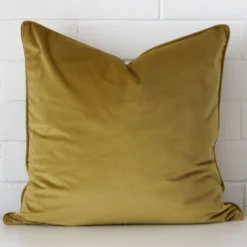 Mustard velvet cushion cover features prominently against a white wall. It is a square design.