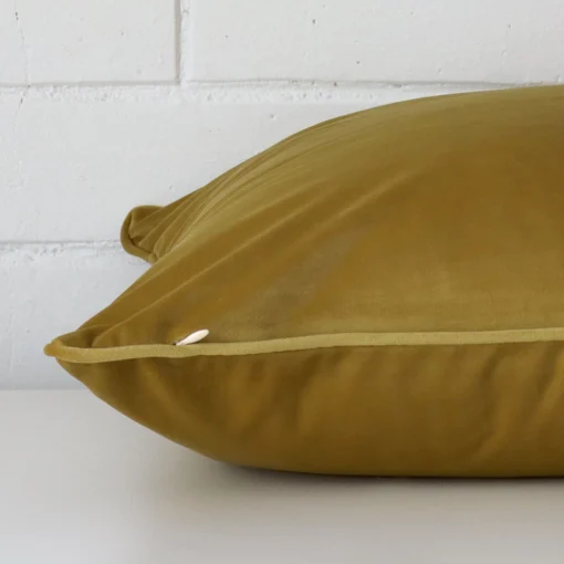 Mustard cushion laid horizontally. This perspective shows the edge of the velvet fabric and its square shape.