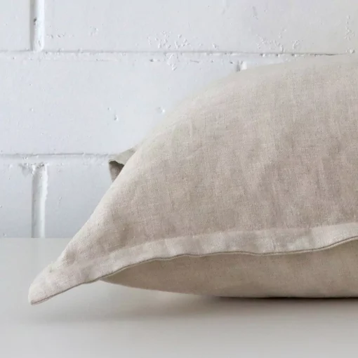 The edge of this linen square cushion in natural is shown. The shot shows the front and rear panels.