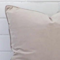 Close up view showing a corner of this velvet cushion in a square size and with natural colouring.