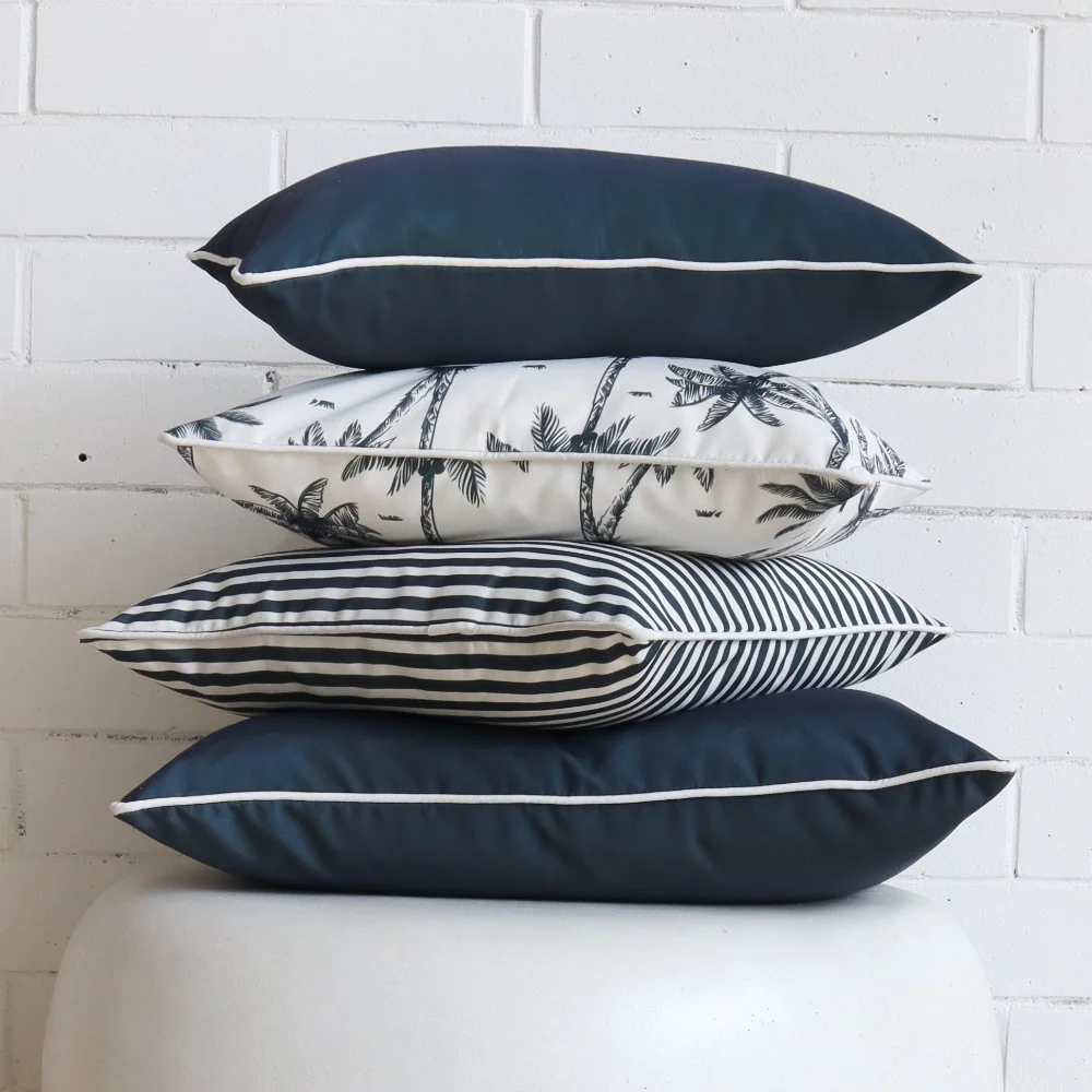 Four navy outdoor cushions are stacked on top of each other in front of a white wall.