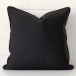 Black cushion cover sits against a white wall. It is constructed from a superior looking linen material and has square dimensions.