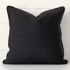 Black cushion cover sits against a white wall. It is constructed from a superior looking linen material and has square dimensions.