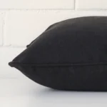 Square cushion cover in black colour sitting flat. The sideways viewpoint shows the seams of the linen material.