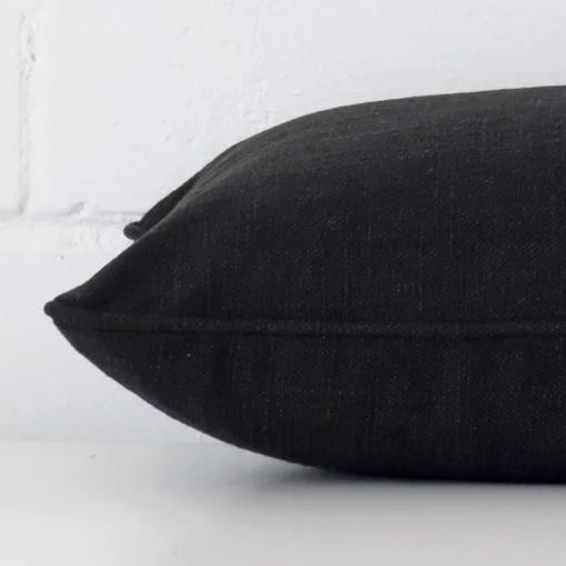 The edge of this linen rectangle cushion in black is shown. The shot shows the front and rear panels.