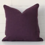 Square cushion cover in plum colour sitting upright in front of a brick wall. It has been made from a quality linen material.