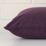 Square plum cushion laid flat. This view shows the linen fabric from side on.