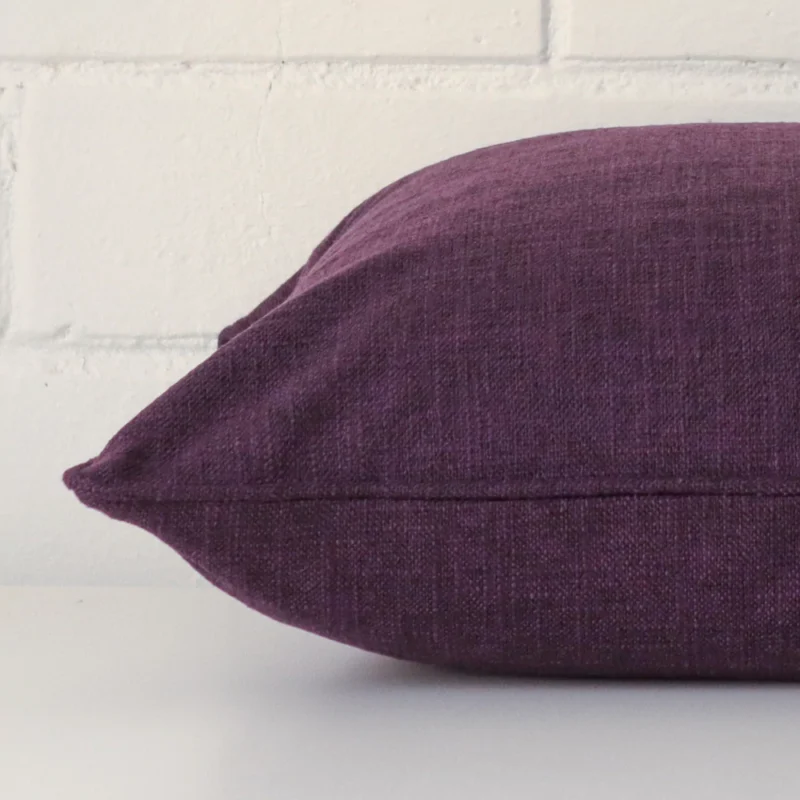 Square plum cushion laid flat. This view shows the linen fabric from side on.