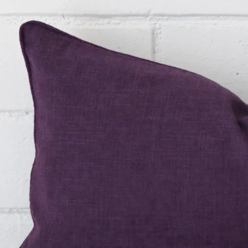 The corner of this plum linen cushion is shown close up. It has a rectangle design.