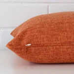 Rust cushion laid horizontally. This perspective shows the edge of the linen fabric and its square shape.