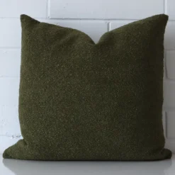 Focused view of square cushion cover. The shot shows details of its linen material and olive green colour.