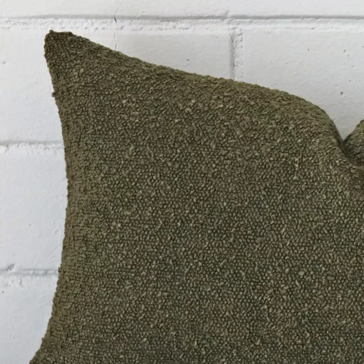 Focused view of rectangle cushion cover. The shot shows details of its boucle material and olive green colour.