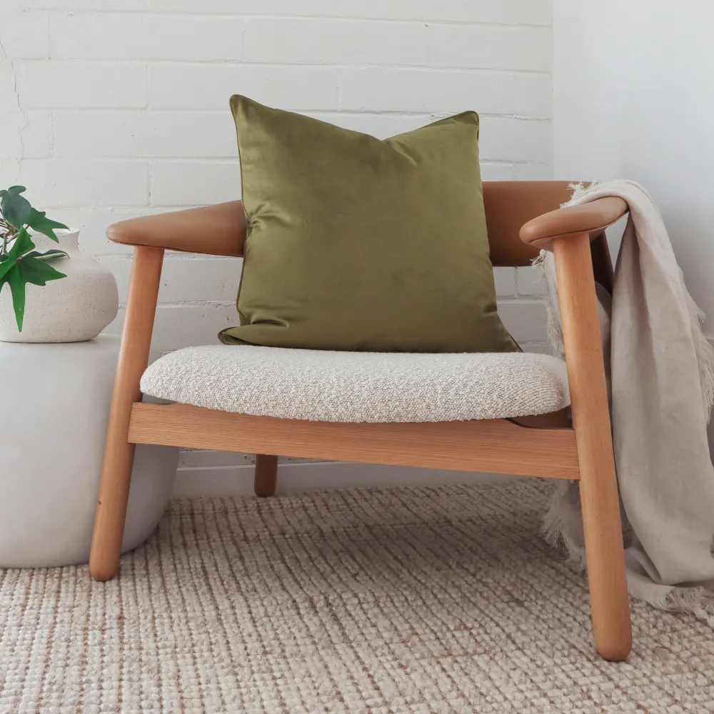 An olive green cushion has been placed on a modern armchair.