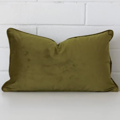 Olive cushion cover in front of a white wall. It has a rectangle size and is made from a velvet material.