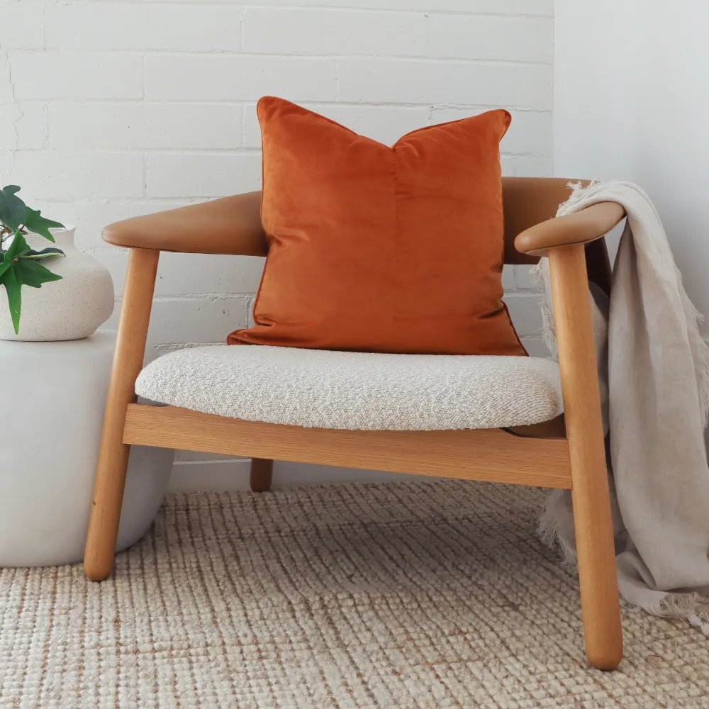 An orange cushion has been placed on a stylish wooden chair with an accompanying throw.