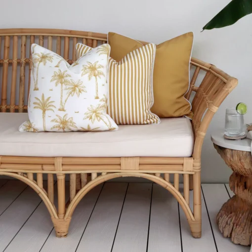 Three mustard-coloured outdoor couch cushions are neatly arranged in a corner of a rattan seat.