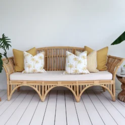 A set of five mustard outdoor cushions sits on a rattan seat nestled against a white wall.