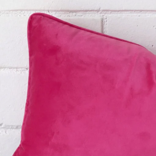 Cropped shot of top left corner of this pink cushion cover. This viewpoint shows the velvet fabric and rectangle shape with more precision.