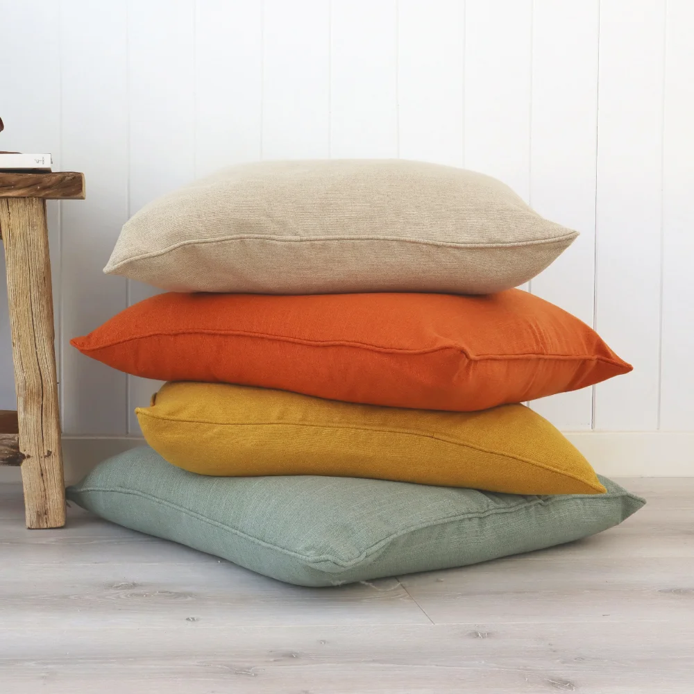 Four plain cushions have been stacked on each other next to a short table.