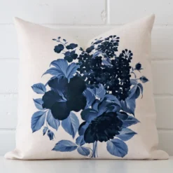 Linen square cushion with a floral design in an upright position against a white brick wall.