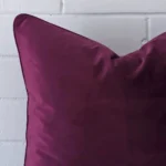 Large cushion in purple colour sitting upright in front of a brick wall. It has been made from a quality velvet material.