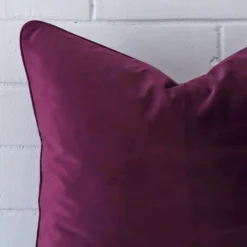 Square cushion in purple colour sitting upright in front of a brick wall. It has been made from a quality velvet material.