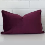 An attractive velvet cushion in front of a white brick wall. It has a rectangle shape and is purple in colour.